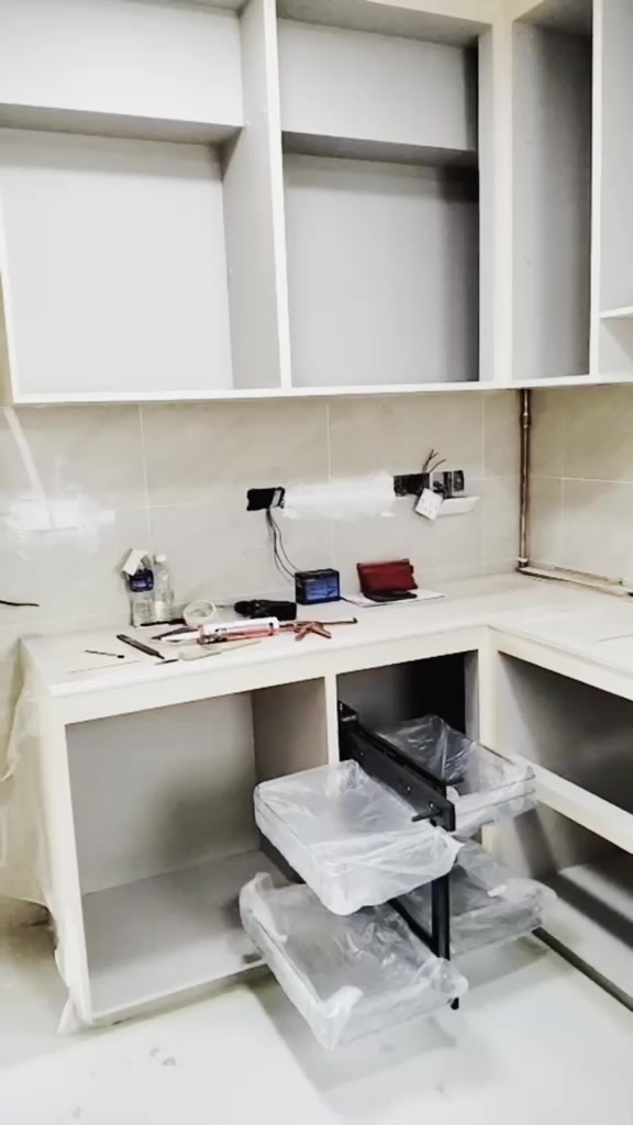 L-shape kitchen mid-installation with upper and lower carcasses in place and a wire pull-out basket fitted